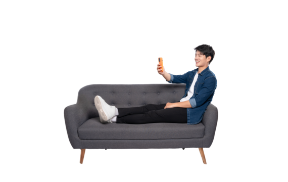 Full body image of young Asian man using phone sitting on sofa on PNG background	