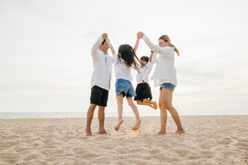 Fototapeta premium Beachside jubilation as an Asian family with father and mother holding children jumps into air. beautiful ocean serves as stunning backdrop highlighting family's happiness and playful bond.