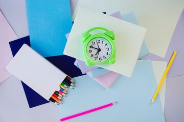 Alarm clock, books, school supplies and creative learning materials in pastel colors, top view,...