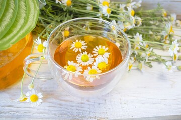 Herbal medicinal tea with chamomile flowers in a glass teapot, a bouquet of fresh flowers, on a...