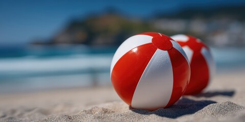 Naklejka premium Two red and white beach balls lie on sandy beach with the ocean and blurred coastline in the background.