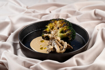 A beautifully plated dish featuring roasted broccoli and mushrooms atop a smooth, savory cream sauce. The elegant presentation highlights the artistic flair of modern gastronomy