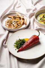 Delicate dishes feature a striking red pepper served on a chic plate alongside flavorful accompaniments. The setting exudes sophistication, perfect for a gourmet experience