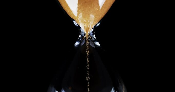 Hourglass. Sands move through hour glass. Sandglass close-up on a black background. Slow motion video. A pile of Golden sand at the bottom of the hourglass, small grains of sand fall from above.