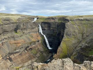 panoramic view of  Grannifoss plummeting off a flat treeless plateau into a canyon showing different geological layers of stone