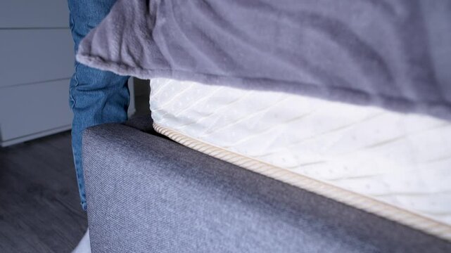 Close-up of a person placing a stack of US dollar bills under a mattress