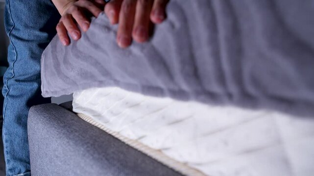 Close-up of a person placing a stack of US dollar bills under a mattress