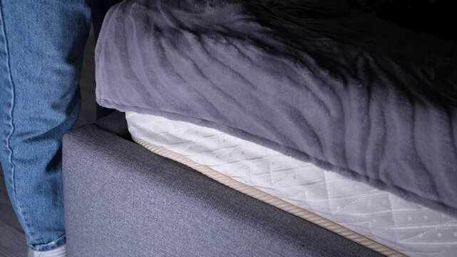Close-up of a person placing a stack of Euro bills under a mattress