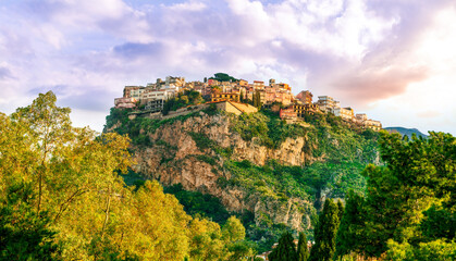 Obraz premium beautiful highland landscape of old town on a top of amazing mountain with green slopes and trees on foreground and amazing blue cloudy sky on background
