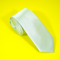 plain fabric necktie rolled on yellow background closeup view 