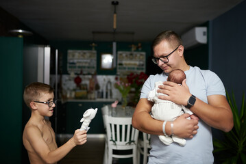 older brother showing newborn baby toy. baby in young father's arms at home
