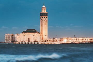 Obraz premium Hassan II Mosque with its minaret towering over the rough waters of the Atlantic Ocean in Casablanca, Morocco, at dusk