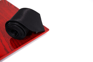 A black tie rolled on wooden frame on white background closeup view 