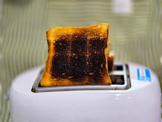  Two burnt toast slices sticking out of modern toaster. Burnt bread from overheating the white...