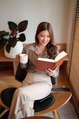 Asian woman enjoys reading book while drinking coffee indoor