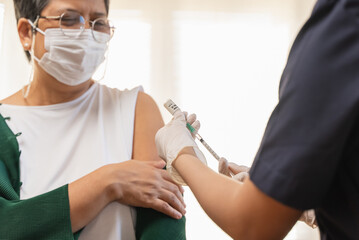 People getting a vaccination to prevent pandemic concept. Mature Woman in medical face mask  receiving a dose of immunization coronavirus vaccine from a nurse at the medical center hospital