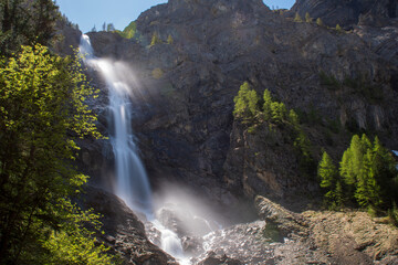 A roaring alpine waterfall crashes over cliffs surrounded by spring bloom. This is Engstligenfälle at its most powerful, fed by snowmelt and spring rains.
