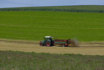 Fototapeta premium Transform your fields with precision! This vibrant image captures a farmer using a modern tractor to spray slurry on a lush green field, ensuring optimal soil fertility. The dynamic composition and ri