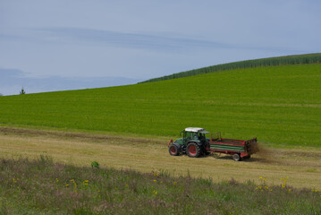 Fototapeta premium Transform your fields with precision! This vibrant image captures a farmer using a modern tractor to spray slurry on a lush green field, ensuring optimal soil fertility. The dynamic composition and ri
