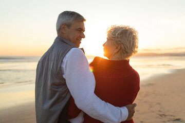 Senior couple embracing on beach at sunset, enjoying retirement
