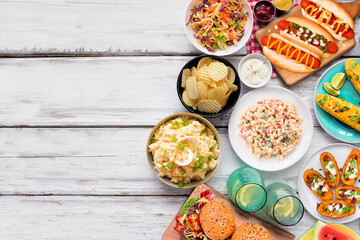 Summer food table scene with hot dogs, hamburger and sides. Overhead view side border over a white wood background. Copy space.