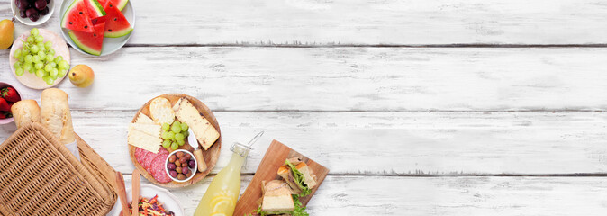 Summer picnic food corner border. Top view over a white wood banner background. Picnic basket, fruit, salad, sandwiches and snacks. Copy space.