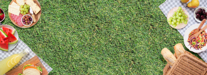 Summer picnic food double border. Top view with blanket over a green lawn banner background. Picnic basket, fruit, salad, sandwiches and snacks. Copy space.
