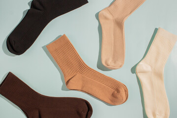 Assorted socks in various colors including brown, beige, and cream, arranged artistically on soft blue background, showcasing texture and style for fashion and apparel marketing