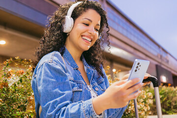 Young woman tourist, with wavy hair, makes a video call using cell phone and listening from wireless headset