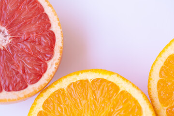 Close-up of juicy orange and grapefruit halves on a soft pink surface, showcasing bright citrus...