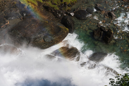 Powerful Norwegian waterfall, top view: turbulent water, ancient rocks, and a bright rainbow in refreshing natural spray.