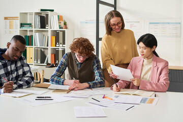 Multiracial group of students and teacher studying foreign languages in well-lit classroom with diverse teaching materials. Collaborative learning environment seen with various study aids around