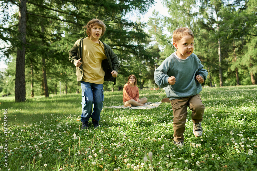 Wall mural full length portrait of two young boys running towards camera on green grass while having fun in par