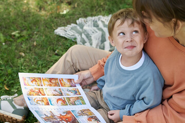High angle closeup of smiling young boy sitting on mothers lap and looking up playfully while...