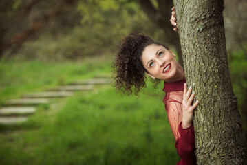 Playful young woman in nature showing expressive face behind tree