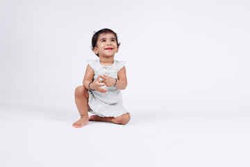 Portrait of a cute little baby girl playing on floor wearing white dress expressing joy and happiness isolated on white background