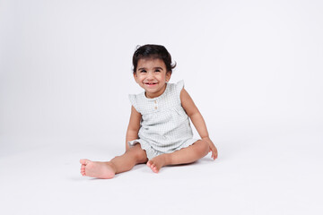 Cute happy little baby girl sitting and playing on floor with happy facial expression wearing white dress isolated on white background