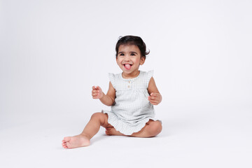 Cute happy little baby girl sitting and playing on floor with happy facial expression wearing white dress isolated on white background
