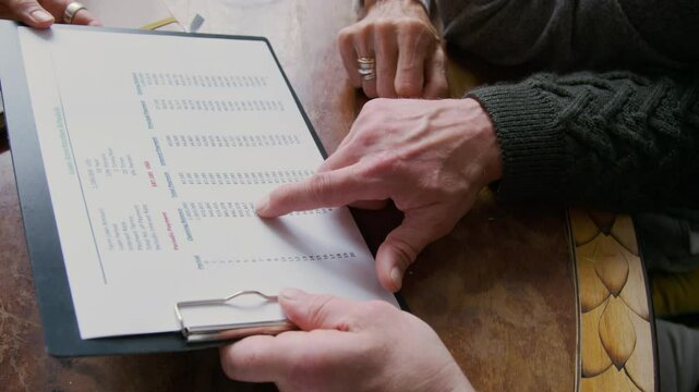 Close-up of hands of unrecognizable female financial consultant demonstrating loan amortization schedule to mature husband and wife, pointing to payment period and interest rates