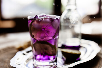 splash purple cocktail with lime garnish on a silver tray, next to a soda bottle. Perfect for drink menus, food styling, or luxury beverage ads with its vibrant allure