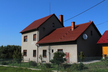 Big grey family house with red tilled roof on blue sky background 