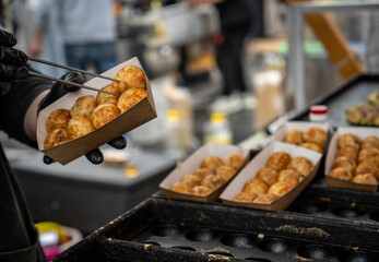 Japanese street food takoyaki being made at a market stall. Cook uses black gloves and skewers to rotate the batter-filled molds until cooked.