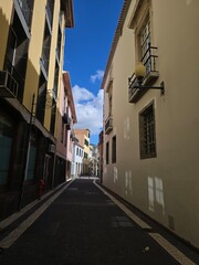 A quiet alleyway in Funchal, Madeira, Portugal, invites visitors to explore its cobbled streets, pastel houses, and timeless southern European charm.