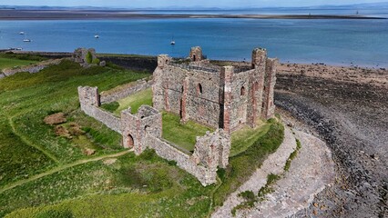 Drone view of medieval castle ruins overlooking the sea with boats and coastline