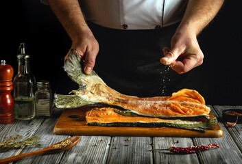 A skilled chef carefully seasons a fillet of salmon with salt in a cozy kitchen. The wooden surface...