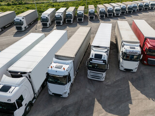 Naklejka na ściany i meble Aerial view of a large truck parking lot at a logistics hub, with multiple commercial semi trucks parked in organized rows.