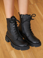 Stylish black lace-up boots complement slim female legs in a cozy interior setting