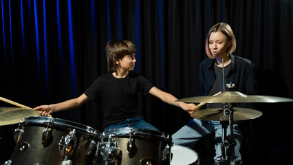 Young caucasian woman teaches a boy to play the drums in the studio on a black background. Music school student