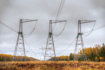 Power transmission line with supports and wires. Wooded area. Autumn, yellow leaves.