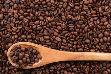 Fototapeta premium Top view of roasted coffee beans and wooden spoon on the table background